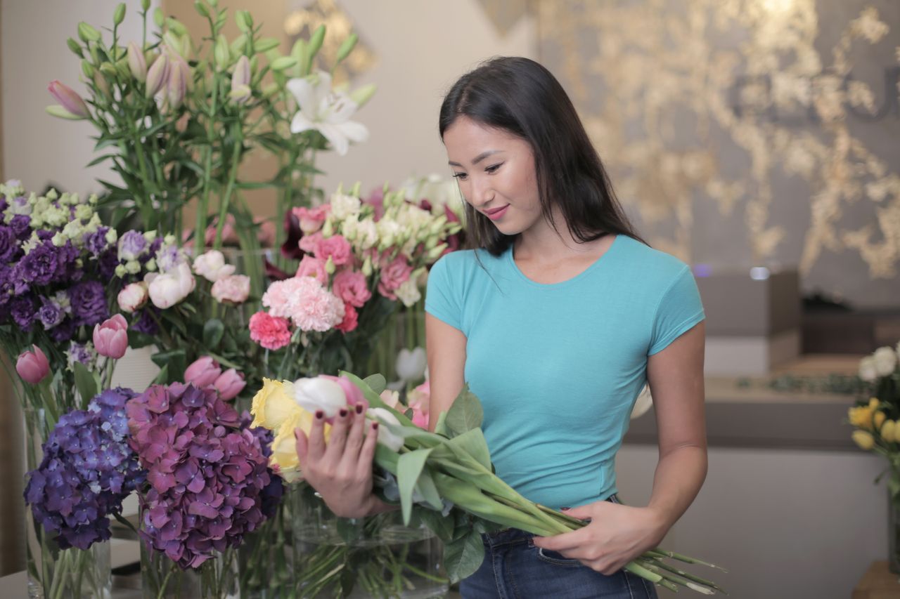 A woman arranging a bouquet in a florist shop surrounded by vibrant flowers, creating an inviting and fresh atmosphere.