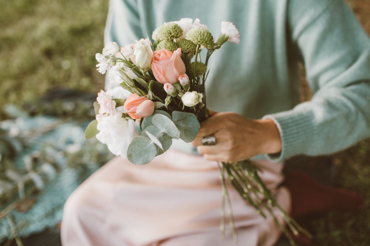 Close-up of a hand holding a pastel flower bouquet outdoors. Perfect for spring themes.