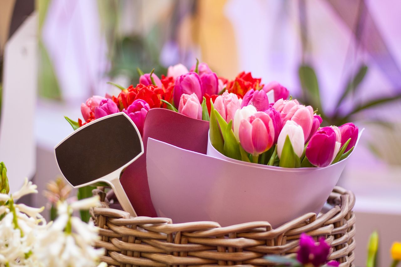 Vibrant pink and red tulips arranged in a woven basket with decorative tags, perfect for brightening any space.